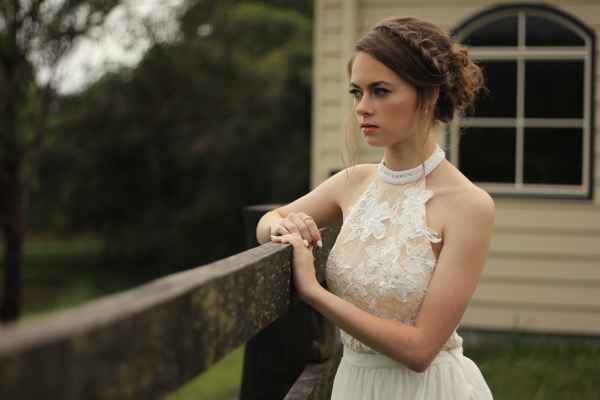 a woman in a white dress leaning on a fence