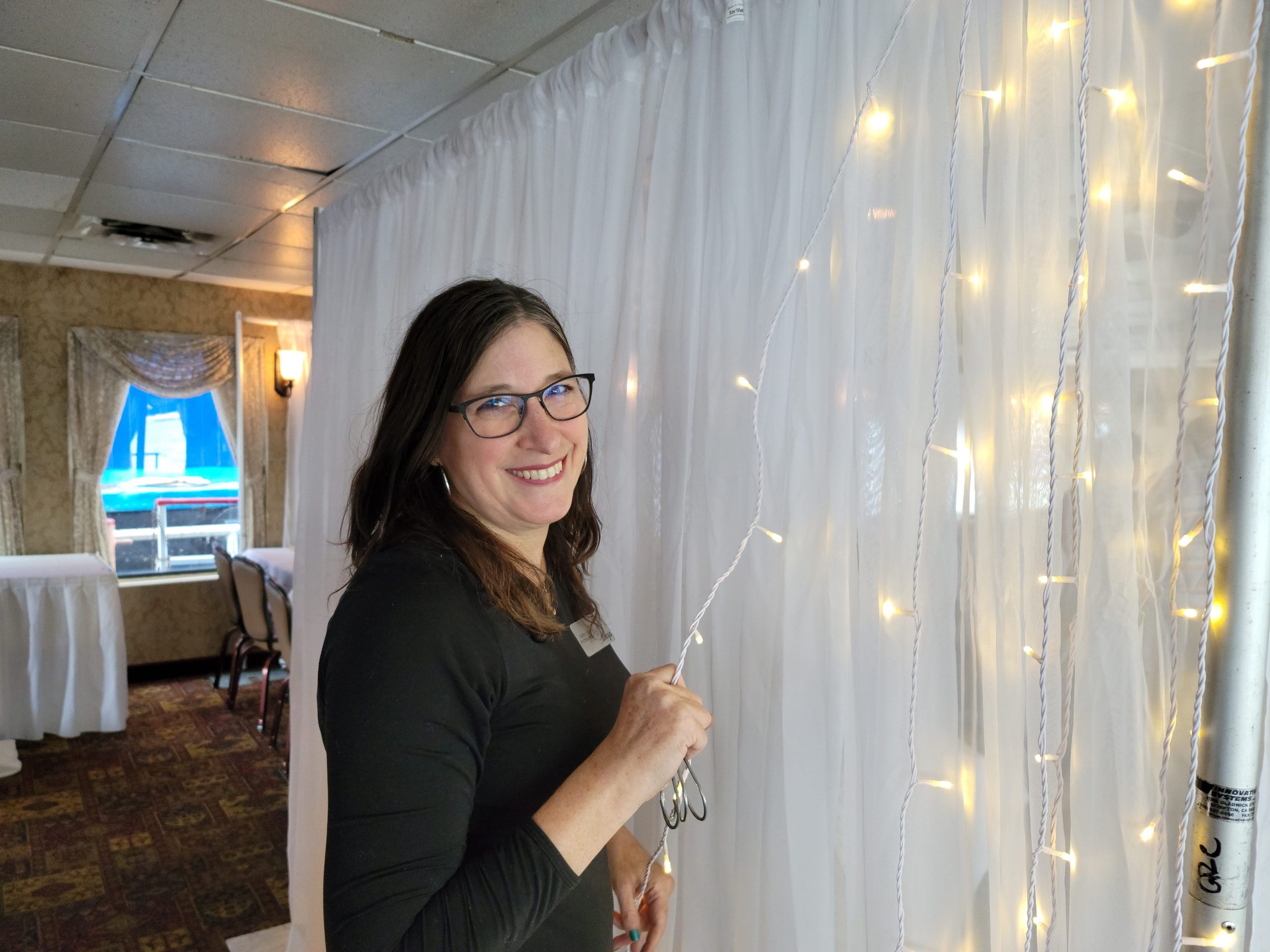 a woman is smiling and holding scissors in front of a curtain